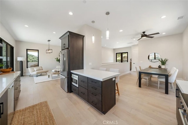 kitchen featuring appliances with stainless steel finishes, a center island, decorative light fixtures, ceiling fan, and light hardwood / wood-style flooring