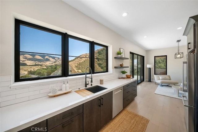 kitchen with light hardwood / wood-style floors, stainless steel appliances, dark brown cabinets, hanging light fixtures, and sink