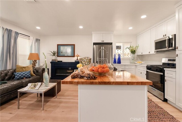 kitchen with butcher block countertops, white cabinetry, a kitchen island, stainless steel appliances, and light hardwood / wood-style floors