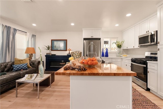 kitchen featuring wooden counters, white cabinets, a center island, stainless steel appliances, and light wood-type flooring