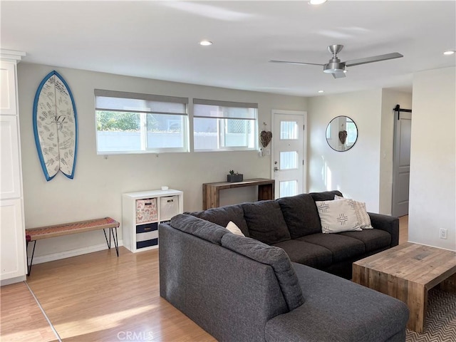 living room with ceiling fan, a barn door, and light hardwood / wood-style floors