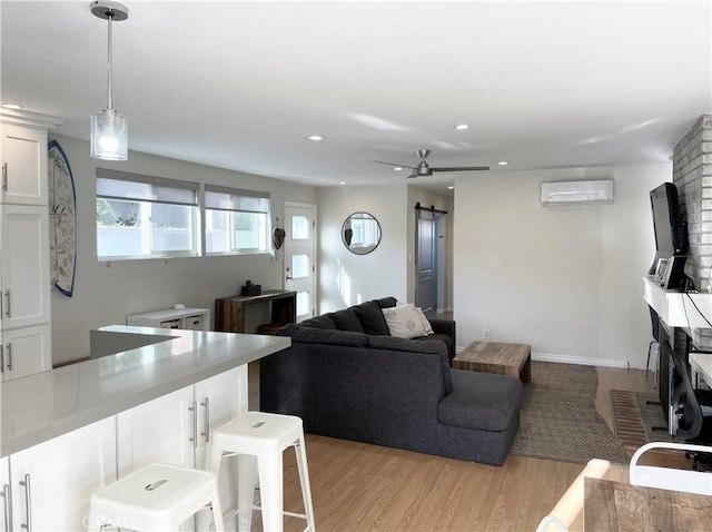 living room with ceiling fan, a barn door, a wall unit AC, and light hardwood / wood-style flooring