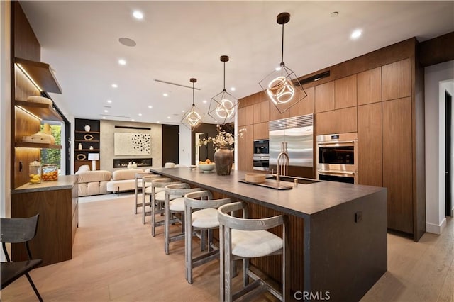 kitchen with built in shelves, a kitchen island with sink, stainless steel built in fridge, and pendant lighting