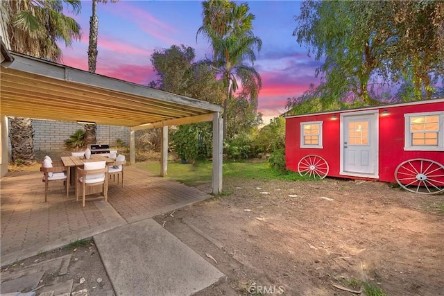 patio terrace at dusk featuring a grill and an outdoor structure