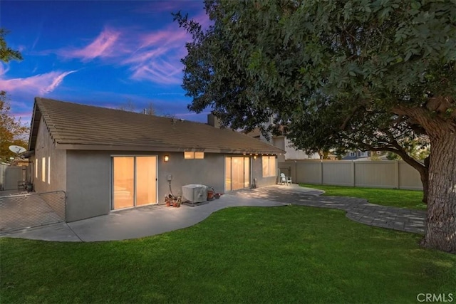 back house at dusk with a patio area and a yard