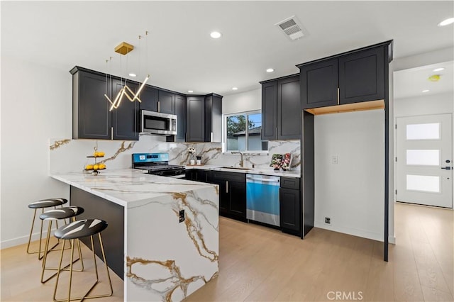 kitchen with light stone countertops, pendant lighting, stainless steel appliances, sink, and kitchen peninsula