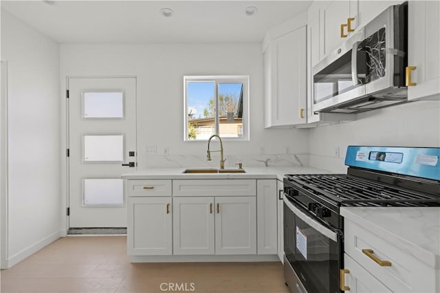 kitchen with light stone countertops, stainless steel appliances, white cabinetry, and sink