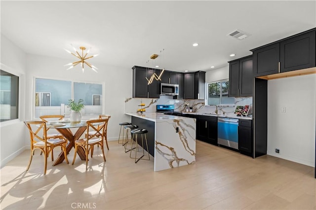 kitchen featuring kitchen peninsula, sink, light stone countertops, appliances with stainless steel finishes, and a kitchen breakfast bar