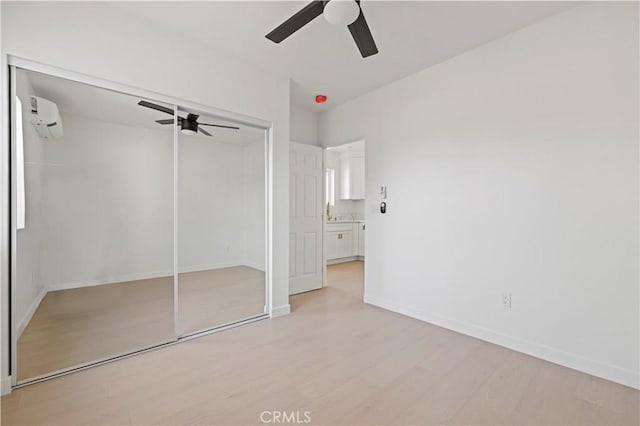 unfurnished bedroom featuring ceiling fan, a closet, an AC wall unit, and light hardwood / wood-style floors