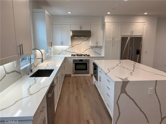 kitchen with white cabinets, appliances with stainless steel finishes, tasteful backsplash, sink, and light stone counters