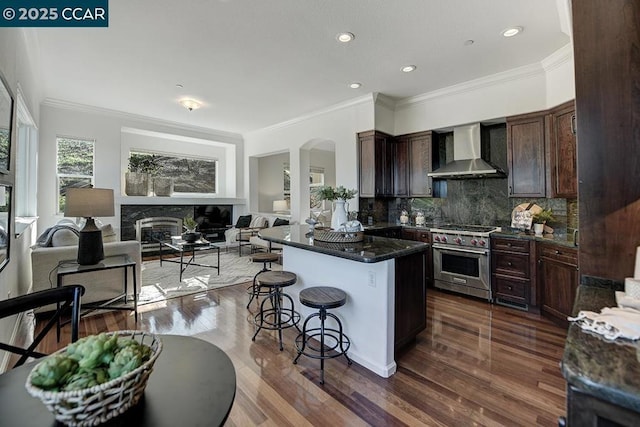 kitchen with luxury stove, wall chimney exhaust hood, tasteful backsplash, ornamental molding, and a breakfast bar