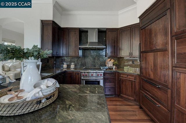 kitchen with wall chimney exhaust hood, dark stone counters, dark hardwood / wood-style floors, decorative backsplash, and high end stove