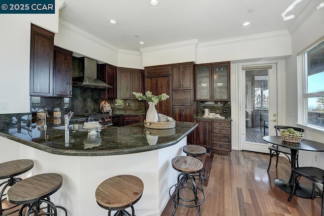 kitchen featuring wall chimney exhaust hood, tasteful backsplash, kitchen peninsula, and dark brown cabinetry