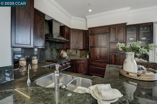 kitchen featuring wall chimney exhaust hood, dark stone counters, tasteful backsplash, sink, and ornamental molding