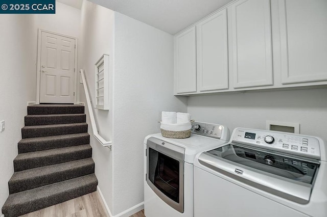 clothes washing area featuring cabinets, washing machine and dryer, and light wood-type flooring