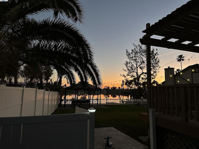 yard at dusk with a gazebo, a patio, and a water view