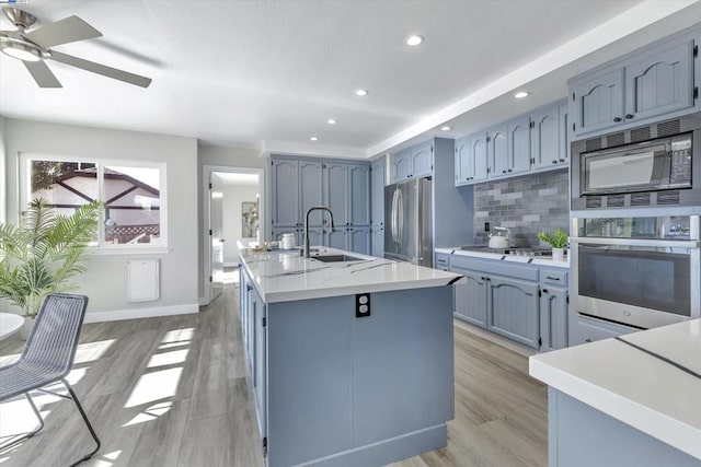 kitchen with stainless steel appliances, sink, light hardwood / wood-style flooring, backsplash, and a kitchen island with sink