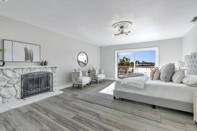 bedroom featuring a notable chandelier, light hardwood / wood-style floors, access to exterior, and a stone fireplace