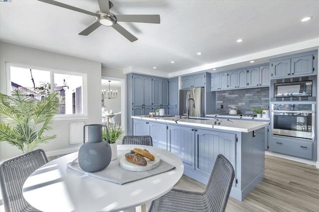 kitchen featuring hardwood / wood-style flooring, backsplash, blue cabinetry, appliances with stainless steel finishes, and sink