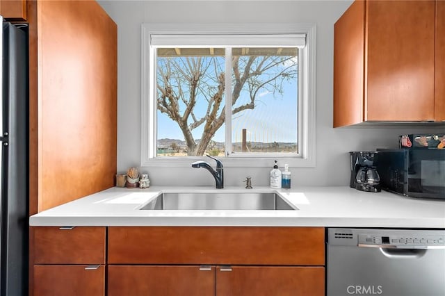 kitchen featuring appliances with stainless steel finishes, brown cabinets, light countertops, and a sink