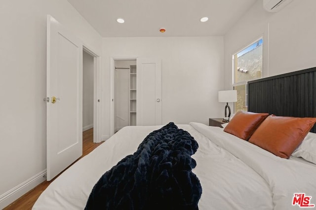 bedroom featuring a walk in closet, wood-type flooring, an AC wall unit, and a closet