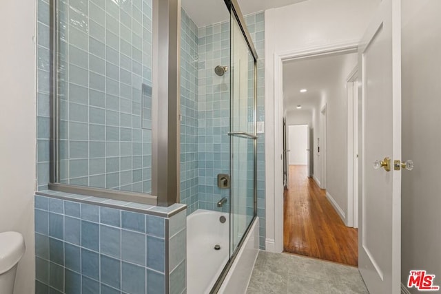 bathroom with toilet and bath / shower combo with glass door