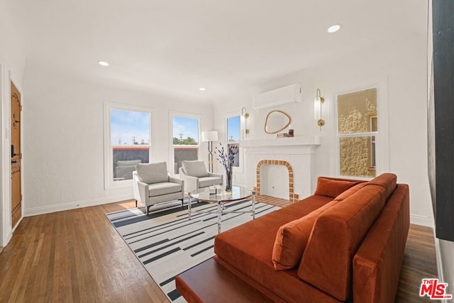 living room featuring a brick fireplace, wood-type flooring, and a wall mounted air conditioner