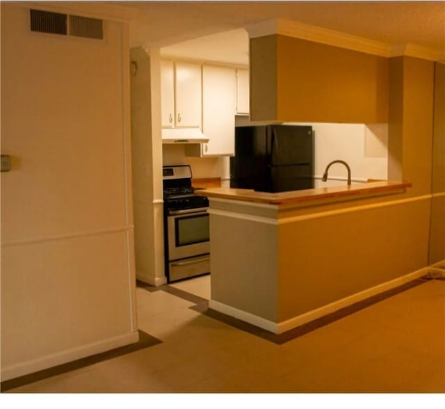 kitchen with white cabinets, black refrigerator, stainless steel range, kitchen peninsula, and ornamental molding