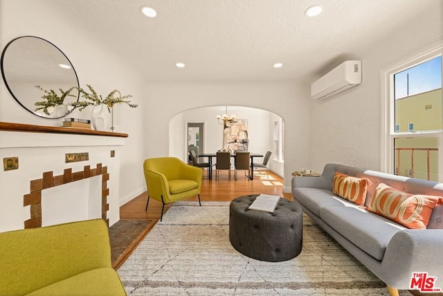 living room featuring a textured ceiling, hardwood / wood-style flooring, an AC wall unit, and a notable chandelier