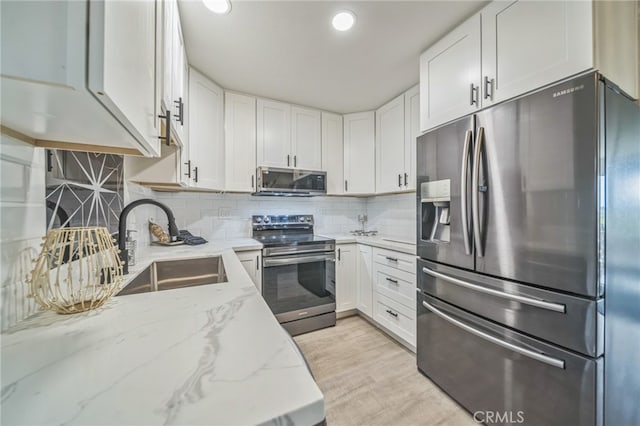 kitchen with tasteful backsplash, sink, white cabinetry, appliances with stainless steel finishes, and light stone counters