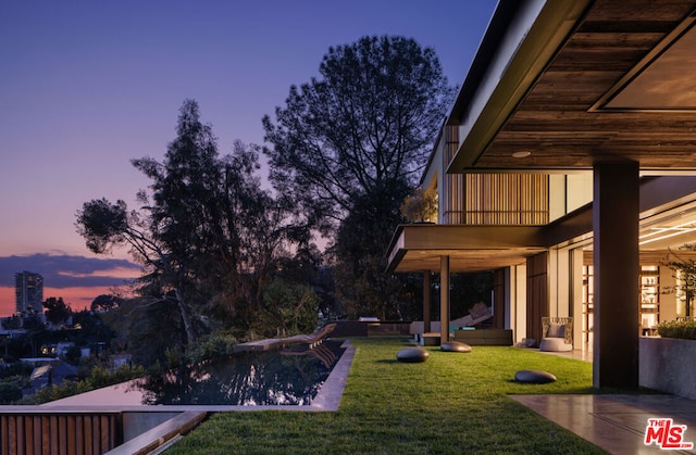 yard at dusk with a pool, a patio area, and a balcony