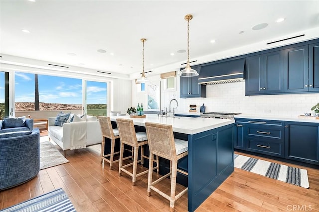 kitchen featuring a center island with sink, blue cabinetry, custom range hood, pendant lighting, and sink