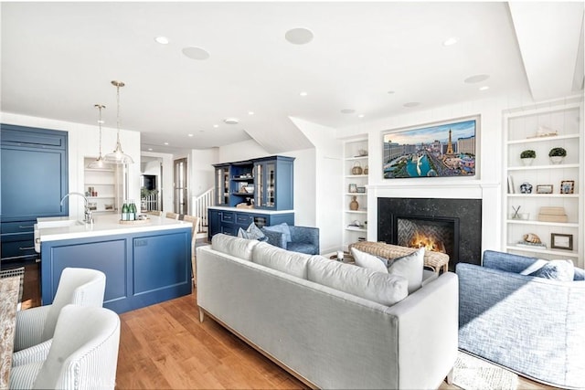 living room featuring a fireplace, built in features, light hardwood / wood-style flooring, and sink