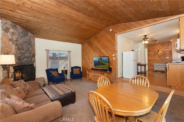 dining space with lofted ceiling, a stone fireplace, wooden walls, ceiling fan, and wooden ceiling