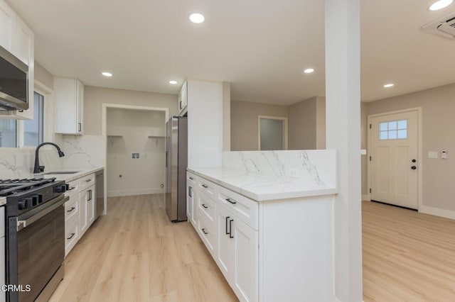 kitchen with white cabinetry, stainless steel appliances, backsplash, light stone countertops, and light hardwood / wood-style flooring