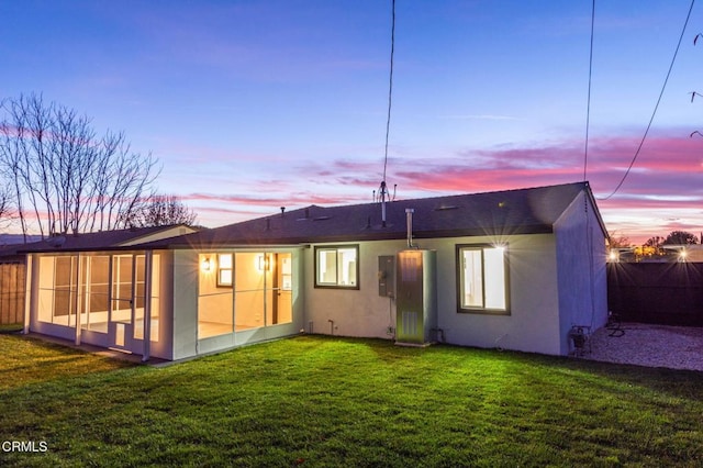 back house at dusk featuring a yard, a sunroom, and electric panel