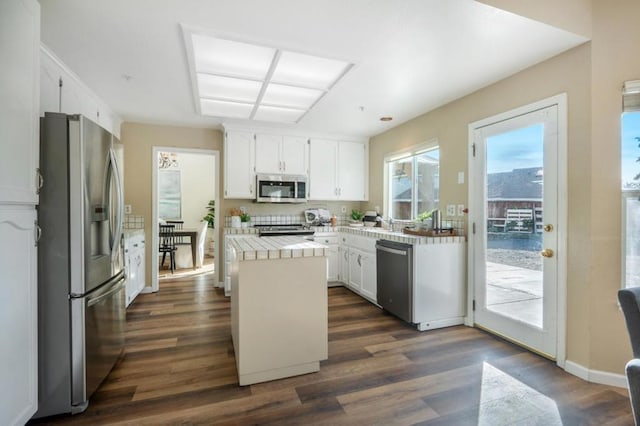 kitchen featuring stainless steel appliances, white cabinetry, tile counters, a kitchen island, and dark wood-type flooring