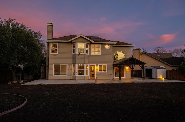 back house at dusk featuring a patio area and a storage shed