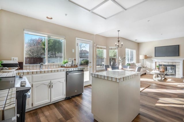 kitchen featuring stainless steel dishwasher, tile counters, decorative light fixtures, a tile fireplace, and white cabinetry