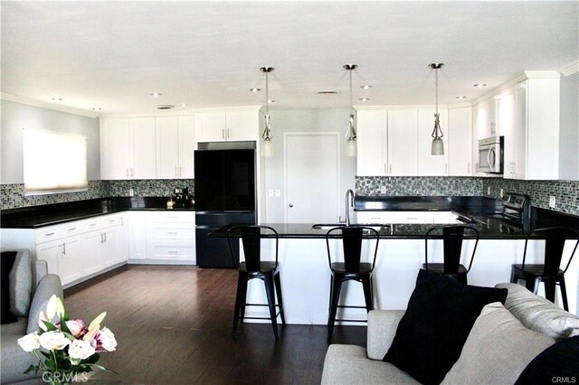 kitchen with appliances with stainless steel finishes, a kitchen bar, white cabinetry, sink, and hanging light fixtures