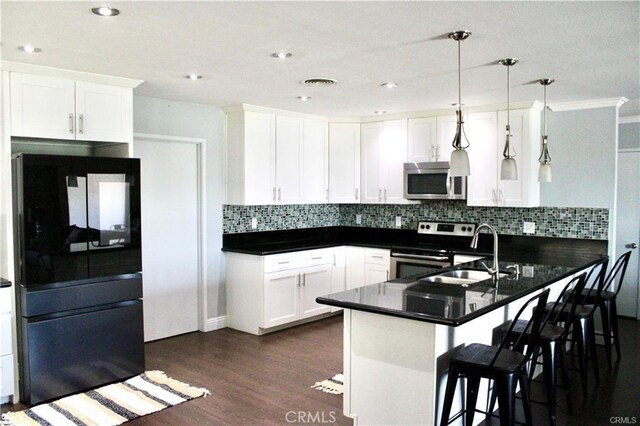 kitchen with appliances with stainless steel finishes, white cabinets, sink, kitchen peninsula, and pendant lighting