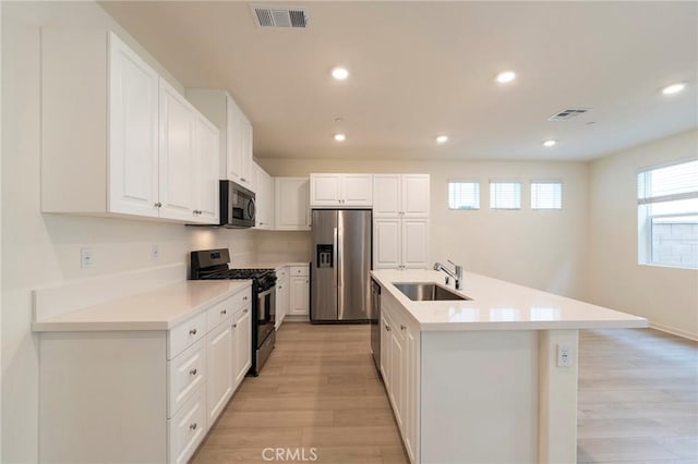 kitchen with white cabinets, stainless steel appliances, sink, a kitchen island with sink, and light hardwood / wood-style flooring