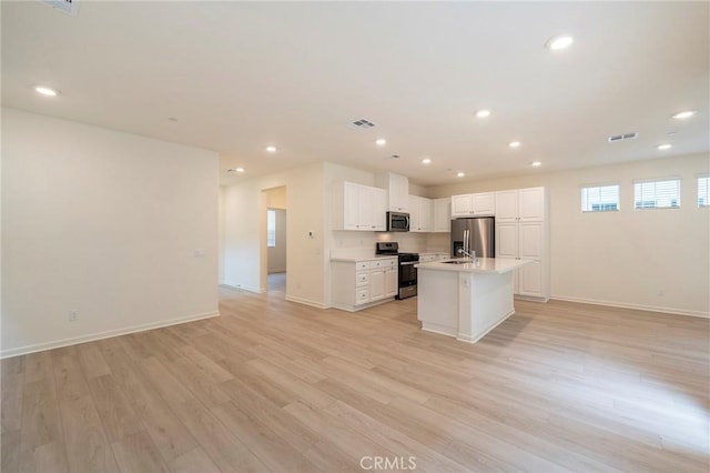 kitchen with appliances with stainless steel finishes, white cabinetry, an island with sink, sink, and light hardwood / wood-style flooring