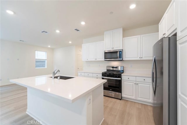 kitchen with a center island with sink, sink, white cabinetry, light hardwood / wood-style flooring, and stainless steel appliances