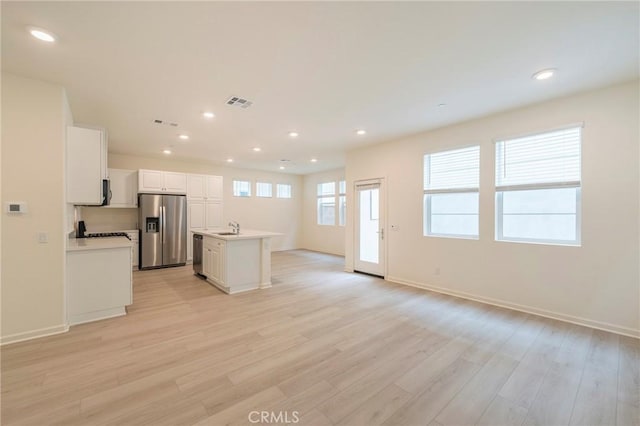 kitchen featuring white cabinets, appliances with stainless steel finishes, sink, light wood-type flooring, and a center island with sink