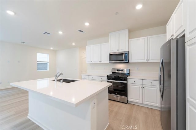 kitchen featuring white cabinets, stainless steel appliances, sink, a kitchen island with sink, and light hardwood / wood-style flooring