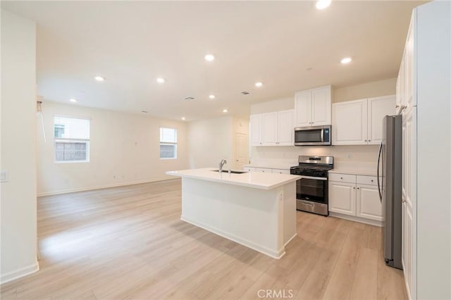 kitchen featuring light wood-type flooring, appliances with stainless steel finishes, white cabinets, and a kitchen island with sink