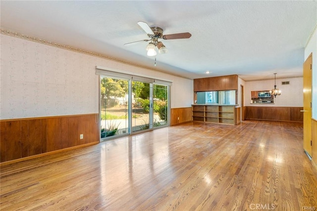 unfurnished living room featuring ceiling fan with notable chandelier and light hardwood / wood-style floors