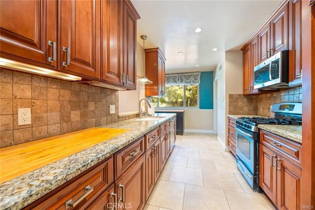 kitchen featuring light stone counters, light tile patterned floors, decorative light fixtures, and appliances with stainless steel finishes