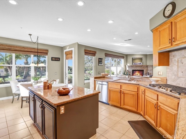 kitchen with a fireplace, tasteful backsplash, appliances with stainless steel finishes, a sink, and light stone countertops